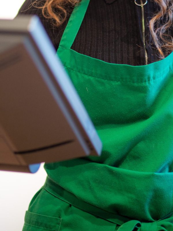 A vertical shot of a happy young female barista with a green apron working the cash register